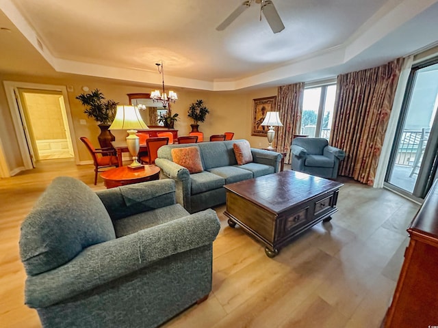 living room with light wood-type flooring, ceiling fan with notable chandelier, and a tray ceiling