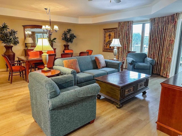 living room with ceiling fan with notable chandelier, light hardwood / wood-style flooring, and a raised ceiling