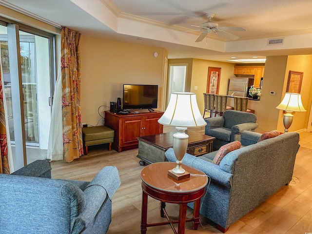 living room featuring a tray ceiling, ceiling fan, light hardwood / wood-style floors, and ornamental molding