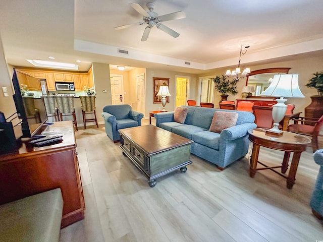 living room with ceiling fan with notable chandelier, light wood-type flooring, and a tray ceiling