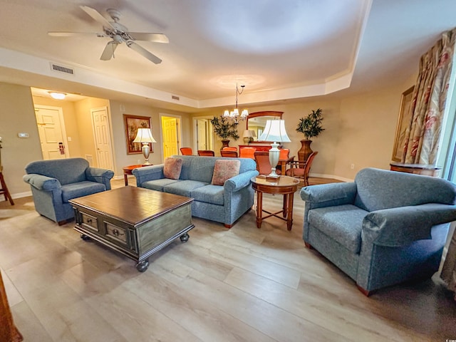 living room featuring ceiling fan with notable chandelier, light hardwood / wood-style floors, and a tray ceiling