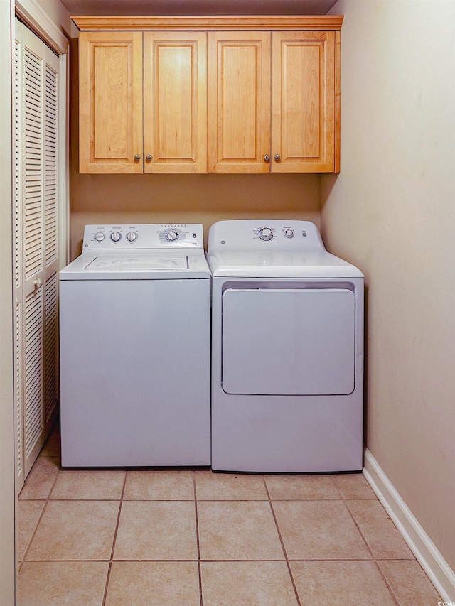 clothes washing area with separate washer and dryer, light tile patterned floors, and cabinets