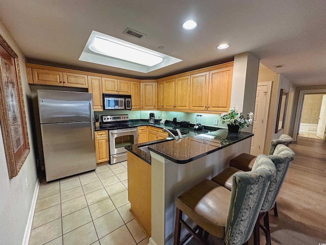 kitchen featuring sink, kitchen peninsula, a breakfast bar area, light tile patterned flooring, and appliances with stainless steel finishes