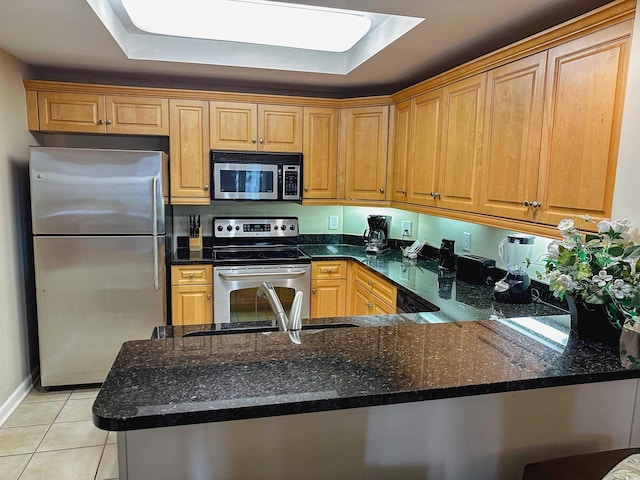 kitchen with kitchen peninsula, dark stone countertops, light tile patterned flooring, and appliances with stainless steel finishes