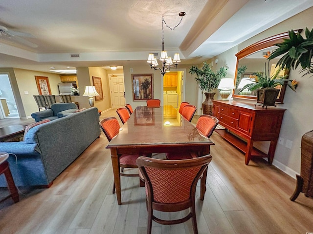 dining area with a raised ceiling, washer and clothes dryer, a chandelier, and light wood-type flooring