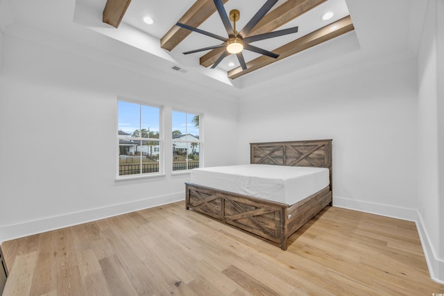 bedroom with a tray ceiling, ceiling fan, wood-type flooring, beamed ceiling, and a high ceiling