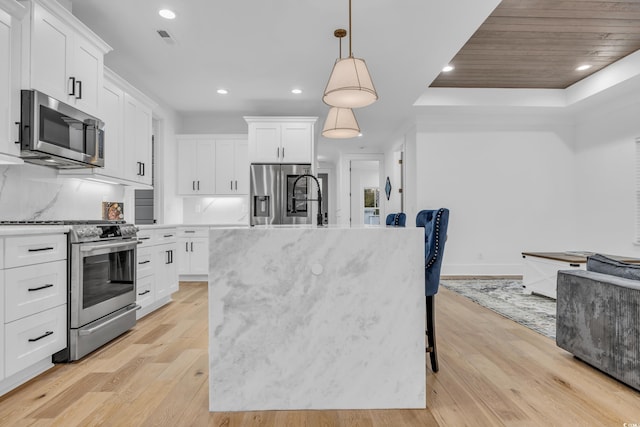 kitchen with pendant lighting, white cabinets, a kitchen island with sink, and appliances with stainless steel finishes