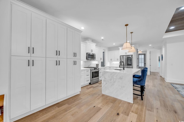 kitchen with a kitchen island with sink, white cabinets, hanging light fixtures, sink, and stainless steel appliances