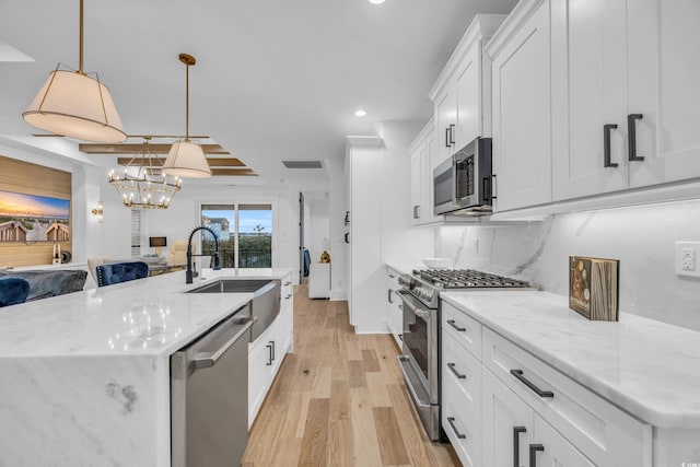 kitchen featuring backsplash, a center island with sink, appliances with stainless steel finishes, decorative light fixtures, and white cabinetry