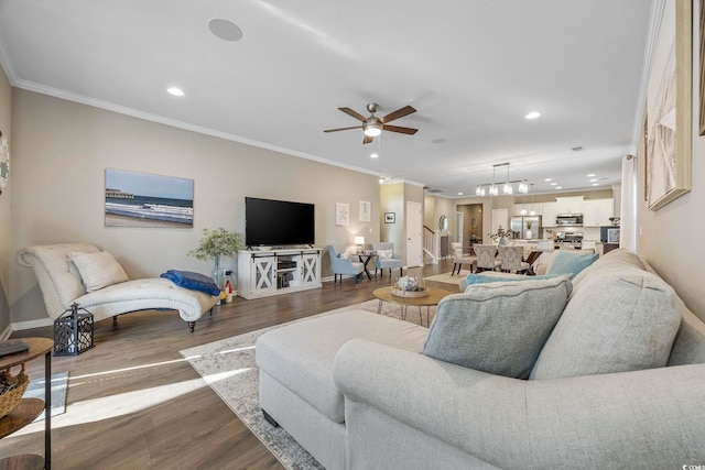 living room with ceiling fan with notable chandelier, wood-type flooring, and ornamental molding