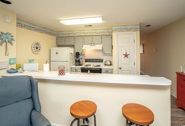 kitchen with kitchen peninsula, white appliances, dark wood-type flooring, and a breakfast bar