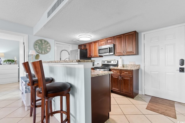 kitchen with a breakfast bar, appliances with stainless steel finishes, a textured ceiling, and light tile patterned floors