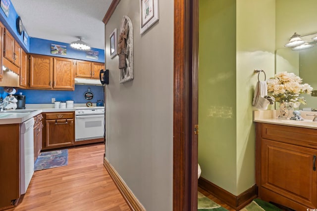 702 Plantation Dr, Surfside Beach, SC 29575 - kitchen with white appliances, under cabinet range hood, a sink, brown cabinetry, and light wood-style flooring