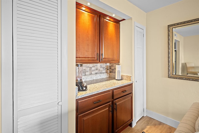 bar featuring decorative backsplash, light stone counters, and light wood-type flooring