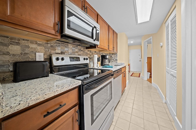 kitchen featuring decorative backsplash, light tile patterned floors, light stone countertops, and appliances with stainless steel finishes