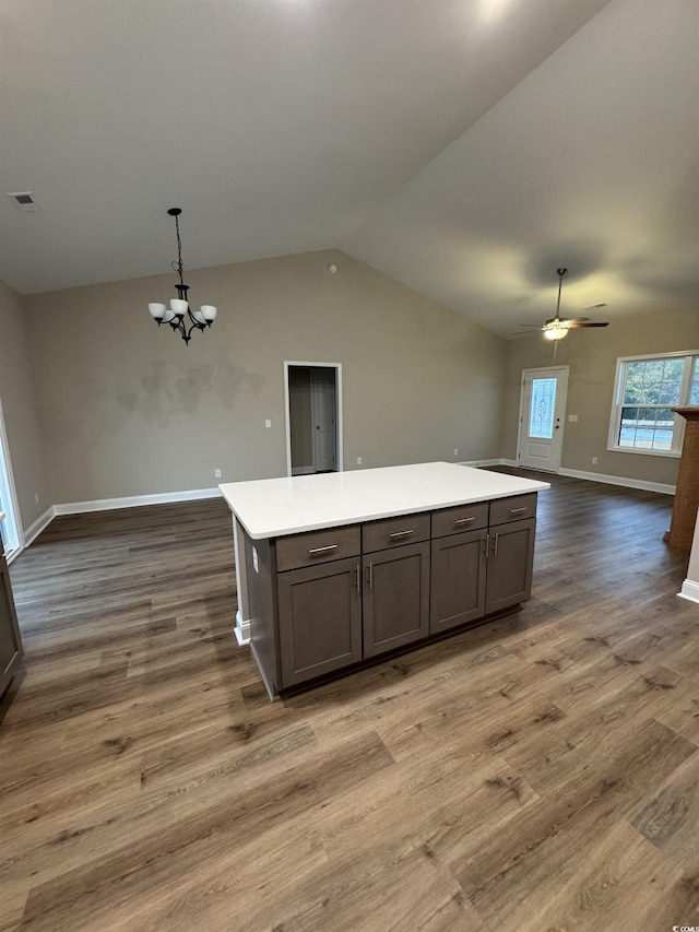 kitchen featuring dark wood-type flooring, hanging light fixtures, vaulted ceiling, a kitchen island, and ceiling fan with notable chandelier