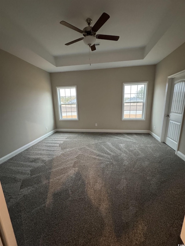 empty room with a tray ceiling, ceiling fan, carpet floors, and a healthy amount of sunlight