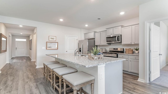 kitchen featuring stainless steel appliances, light stone counters, a kitchen bar, gray cabinets, and a center island with sink