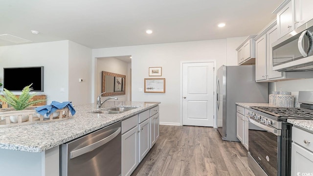 kitchen with light stone counters, stainless steel appliances, sink, a center island with sink, and light hardwood / wood-style floors