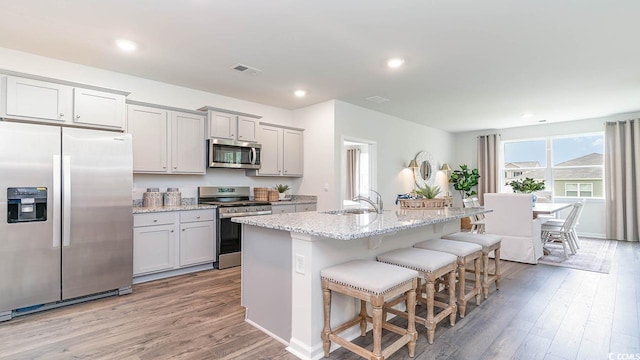 kitchen featuring a kitchen bar, a center island with sink, sink, light stone counters, and stainless steel appliances