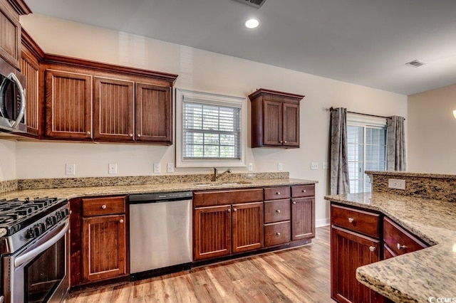 kitchen featuring stainless steel appliances, light stone countertops, sink, and light wood-type flooring