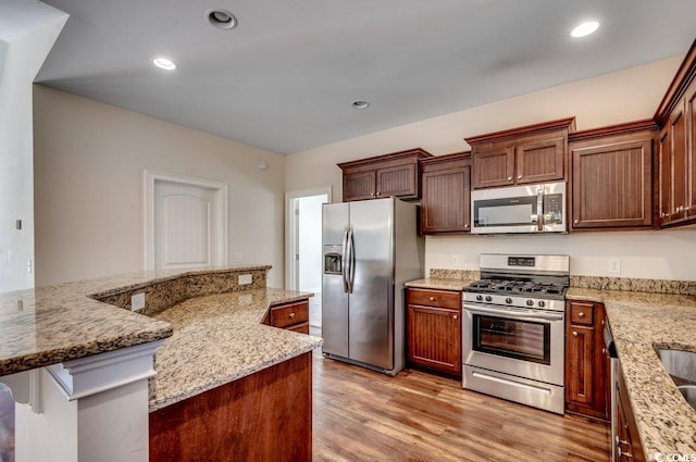 kitchen with appliances with stainless steel finishes, light stone countertops, and light hardwood / wood-style flooring