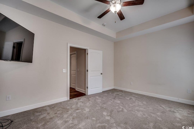 carpeted spare room with a raised ceiling and ceiling fan