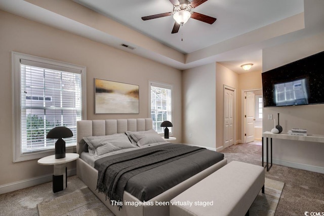 bedroom featuring ensuite bathroom, a tray ceiling, and light carpet