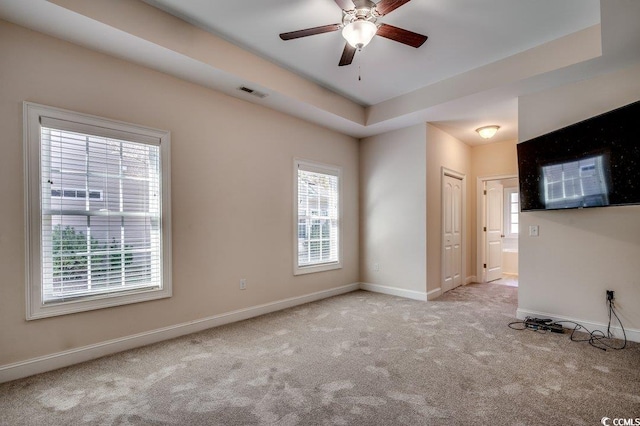 empty room featuring a raised ceiling, light carpet, and ceiling fan