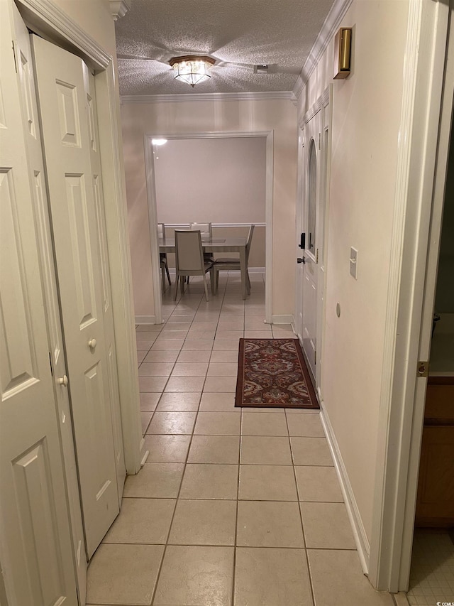 hallway with ornamental molding, a textured ceiling, and light tile patterned floors