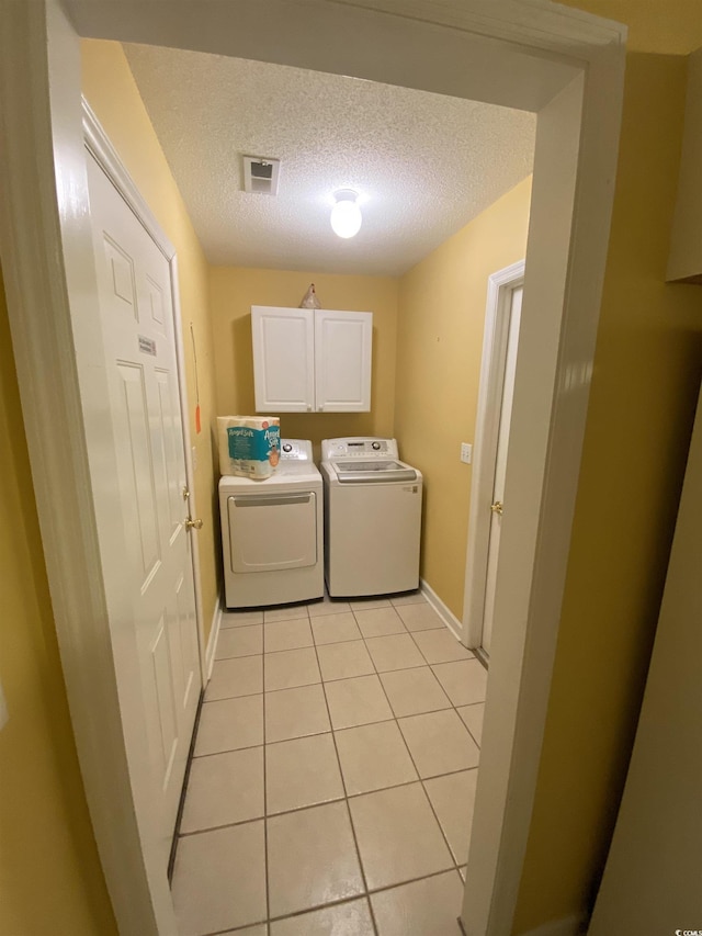 washroom with cabinets, separate washer and dryer, a textured ceiling, and light tile patterned floors