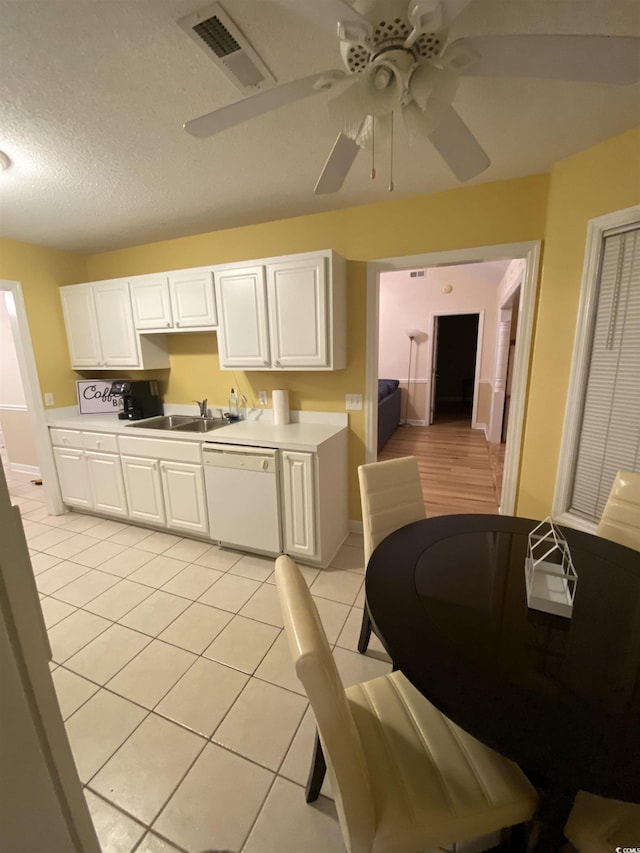 kitchen with white dishwasher, sink, light tile patterned floors, a textured ceiling, and white cabinetry