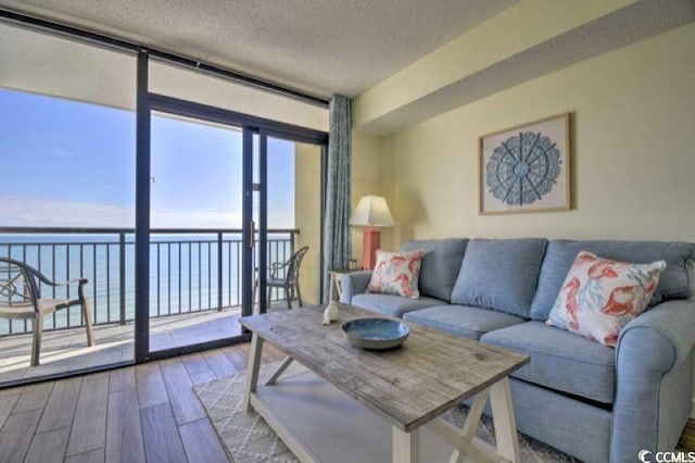 living room with a textured ceiling, a water view, floor to ceiling windows, and hardwood / wood-style flooring