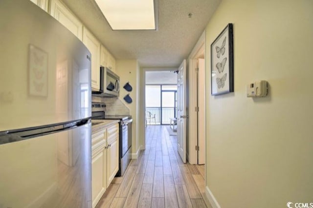 kitchen with white cabinets, light wood-type flooring, a wall of windows, and stainless steel appliances