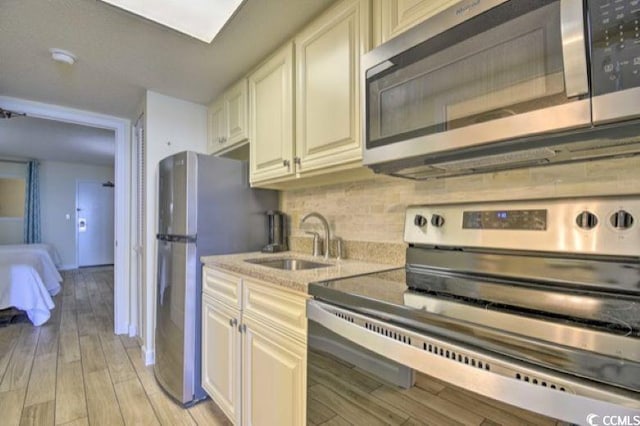 kitchen with tasteful backsplash, sink, appliances with stainless steel finishes, and light hardwood / wood-style flooring