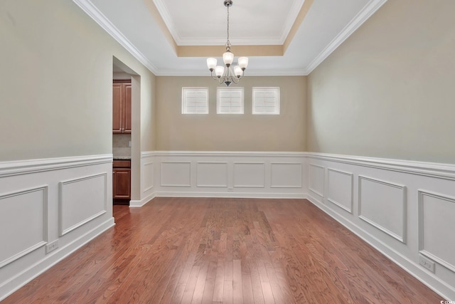 unfurnished room with a tray ceiling, ornamental molding, wood-type flooring, and a notable chandelier