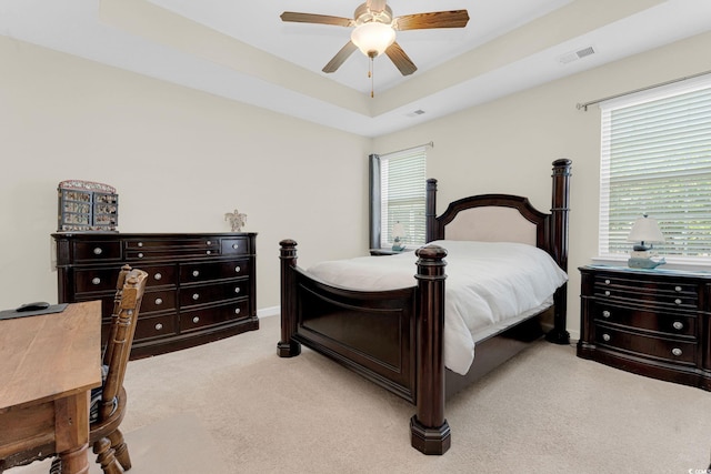 bedroom with ceiling fan, a raised ceiling, light carpet, and multiple windows