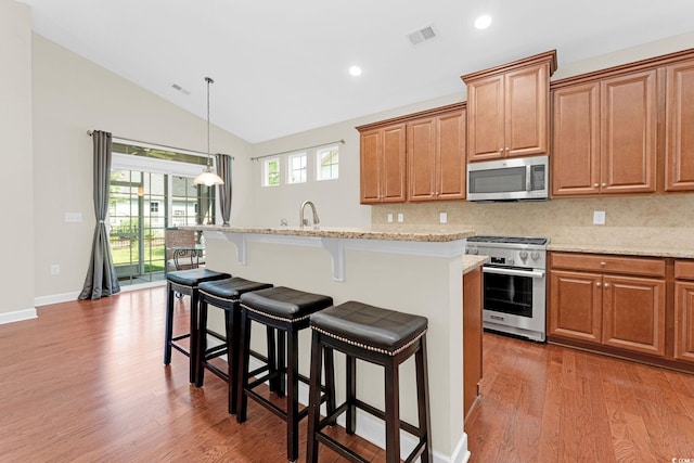 kitchen featuring appliances with stainless steel finishes, backsplash, a center island with sink, and light stone counters