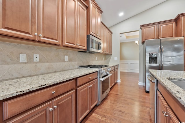 kitchen featuring decorative backsplash, light stone counters, stainless steel appliances, light hardwood / wood-style flooring, and lofted ceiling