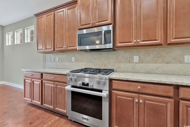 kitchen with light wood-type flooring, light stone countertops, backsplash, and appliances with stainless steel finishes