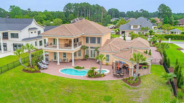 rear view of house featuring a tiled roof, a yard, a balcony, a fenced backyard, and a patio