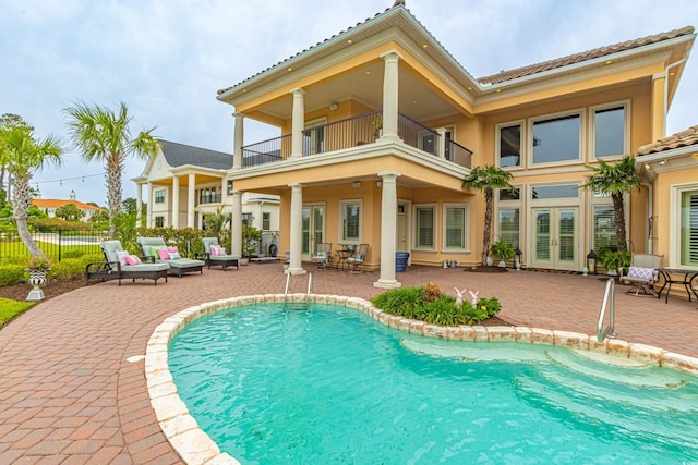 rear view of property featuring stucco siding, a patio, fence, french doors, and a balcony