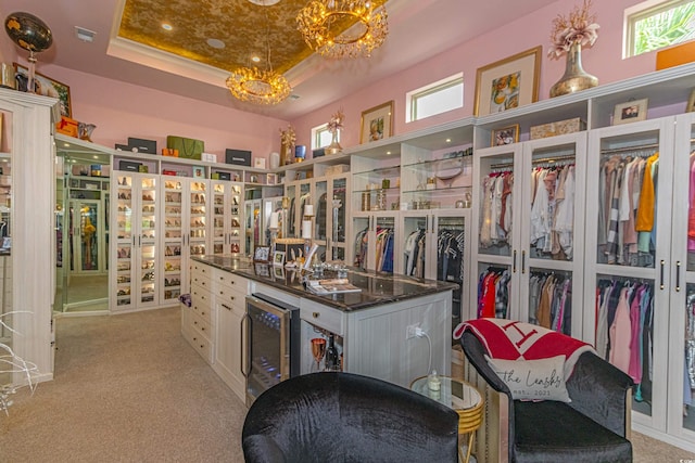 walk in closet featuring a tray ceiling, light carpet, a notable chandelier, and beverage cooler