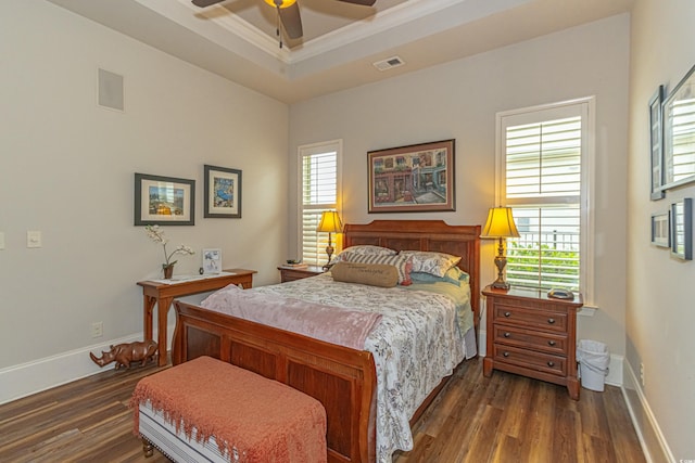 bedroom with dark wood finished floors, visible vents, baseboards, and a tray ceiling