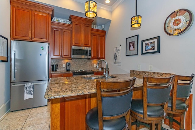 kitchen featuring a breakfast bar area, a peninsula, a sink, appliances with stainless steel finishes, and backsplash