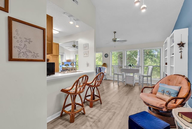 living area with a ceiling fan, baseboards, vaulted ceiling, and light wood finished floors