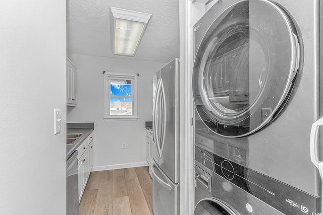 washroom featuring laundry area, baseboards, stacked washer / dryer, a textured ceiling, and light wood-style floors