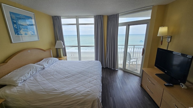 bedroom with access to exterior, a textured ceiling, floor to ceiling windows, and dark wood-type flooring