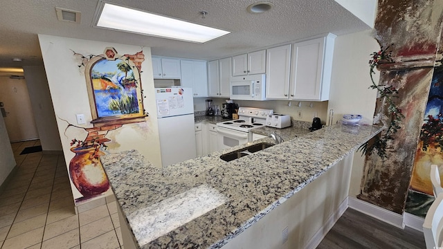 kitchen with kitchen peninsula, light stone countertops, white appliances, sink, and white cabinetry