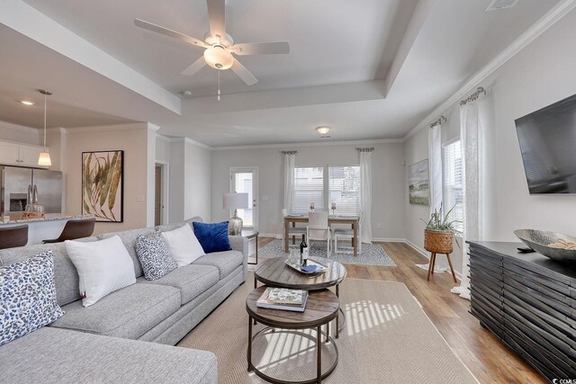 living area with light wood-style flooring, ceiling fan, crown molding, and a raised ceiling